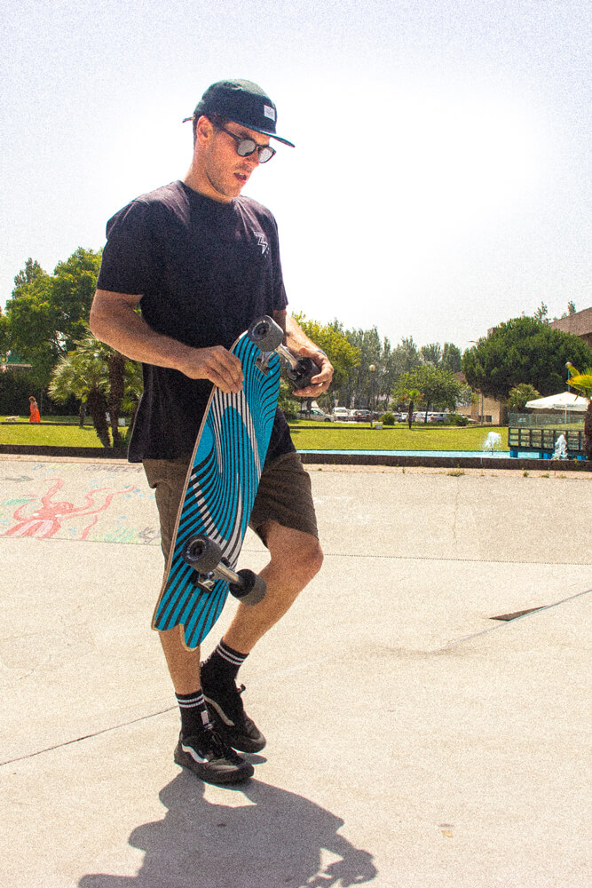 Craig walking on a skatepark holding the curfboard Fish